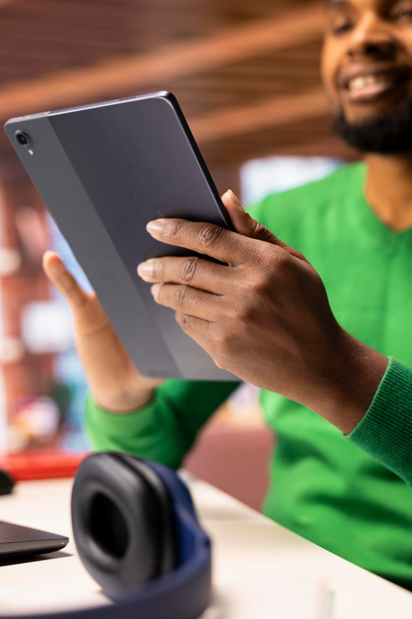 A smiling man in a green sweater reading a tablet at a shared workspace