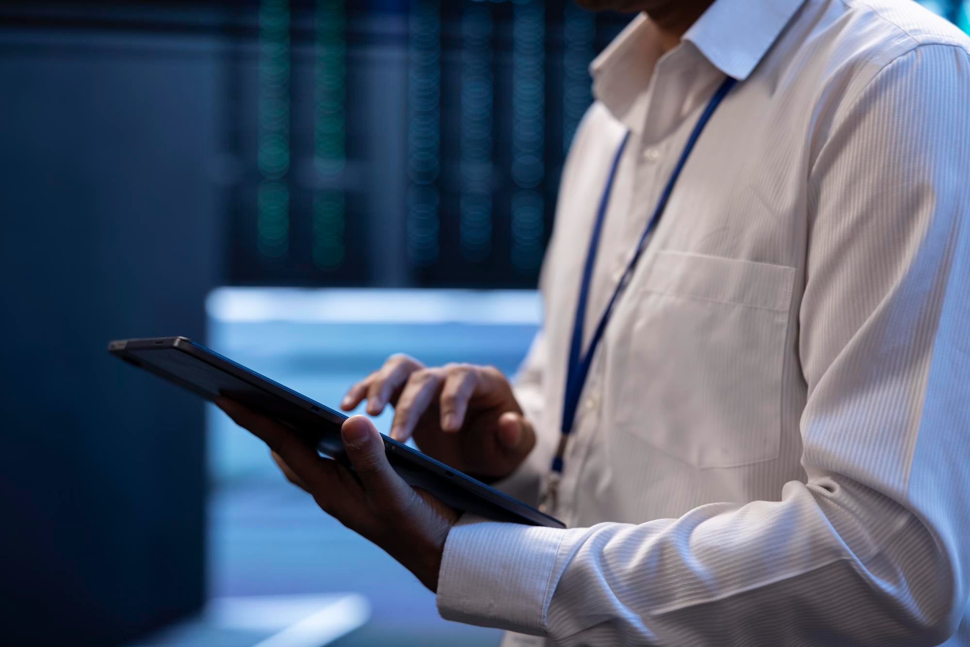 A man with a lanyard using a tablet between server racks
