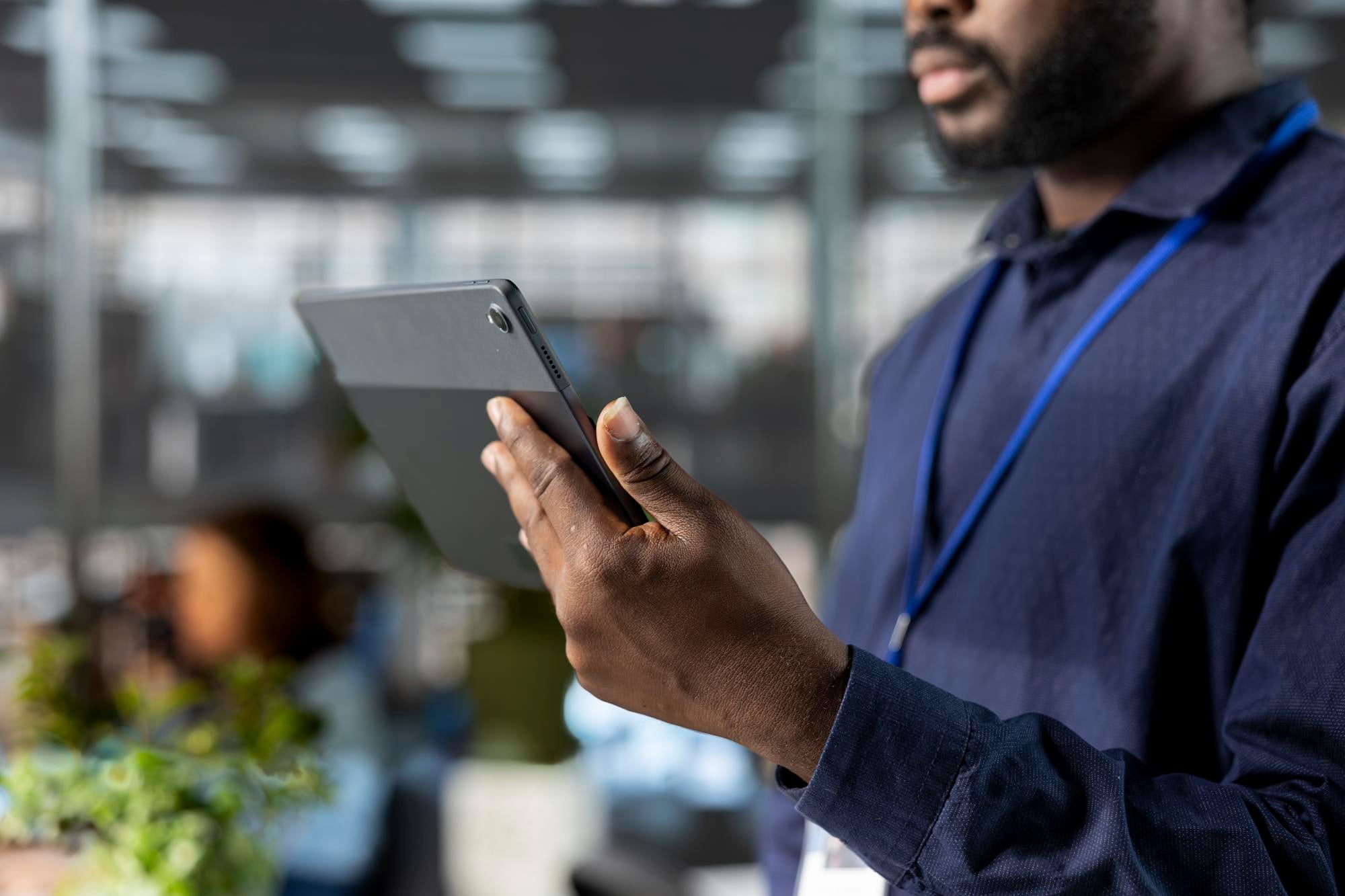 A staff member with a blue lanyard checking a tablet in an open-plan office